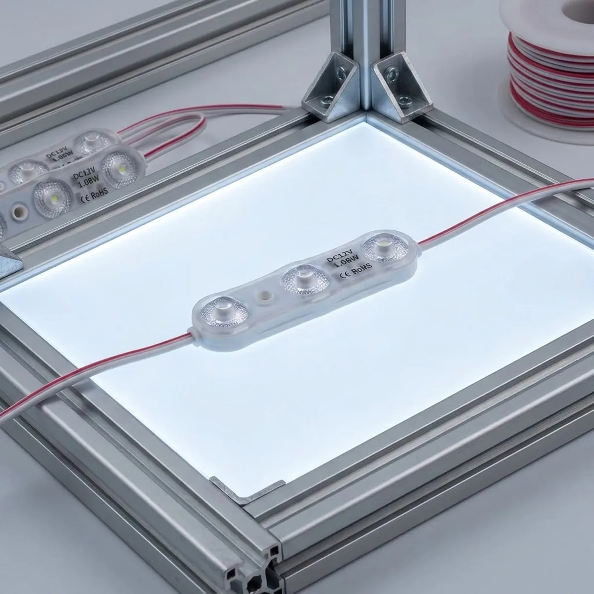 Módulo LED 12V 1,1W de 3 diodos en blanco puro 6000K sobre una caja de luz encendida con perfil de aluminio y cable rojo